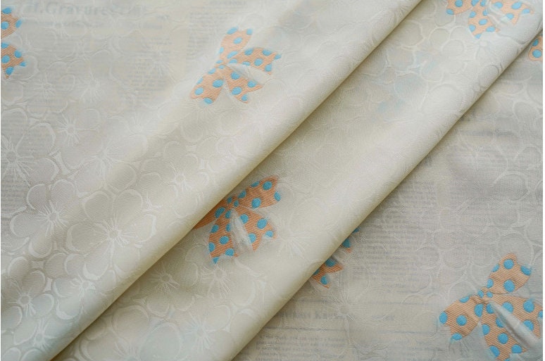 Tissu satin jacquard ivoire : motif nœud papillon, soyeux et lisse (165 cm de large)