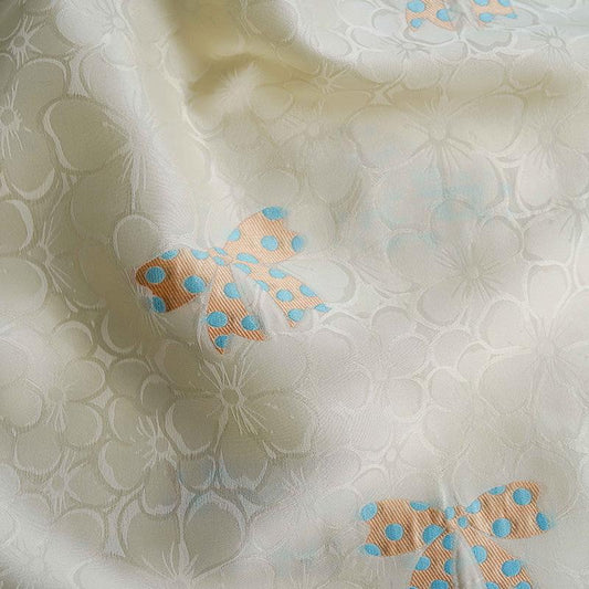 Tissu satin jacquard ivoire : motif nœud papillon, soyeux et lisse (165 cm de large)