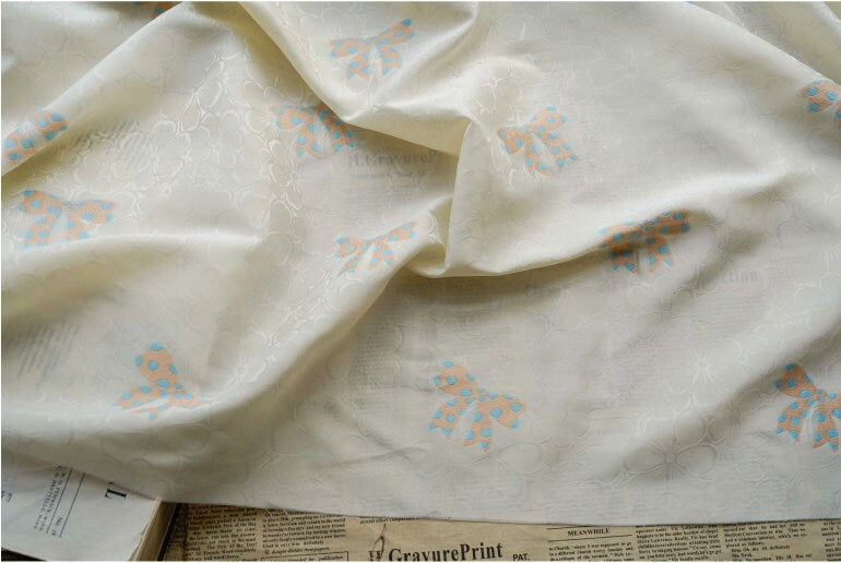 Tissu satin jacquard ivoire : motif nœud papillon, soyeux et lisse (165 cm de large)